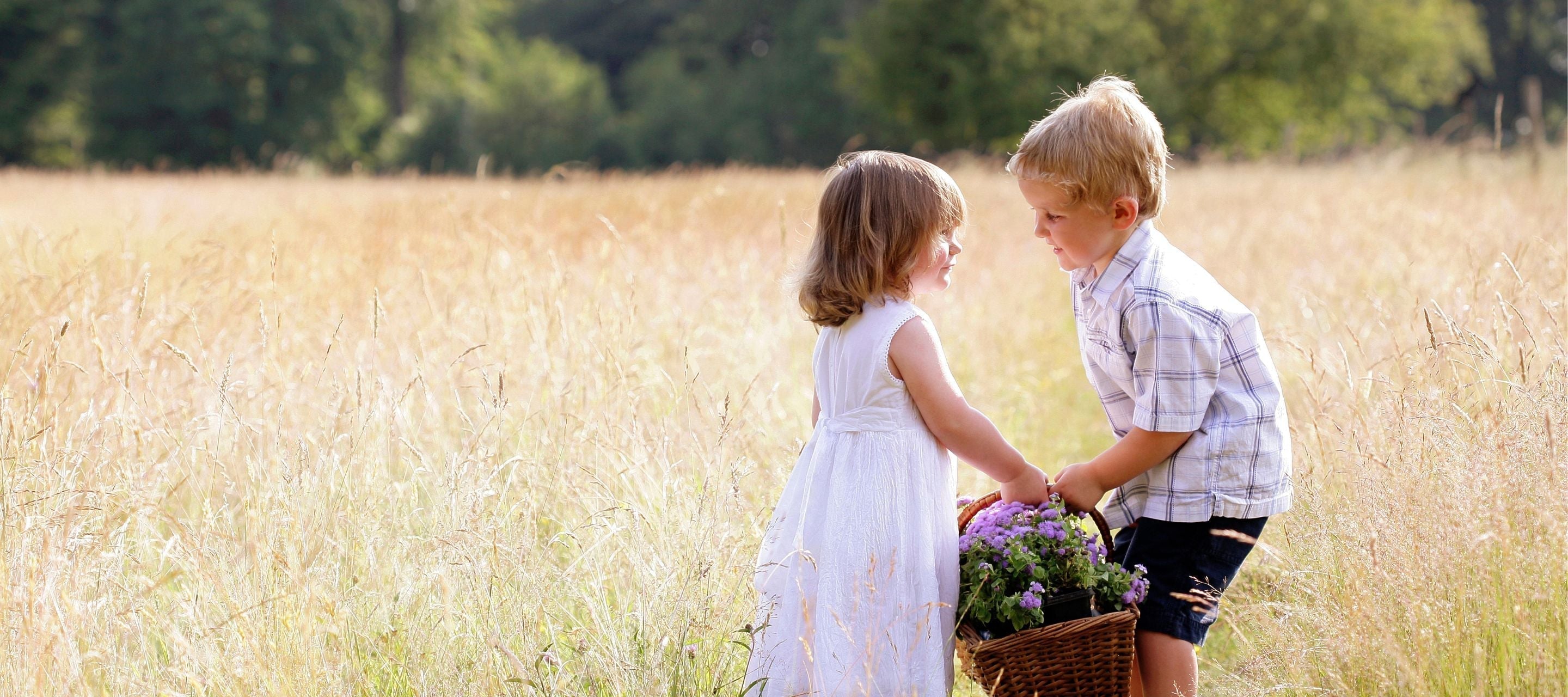 Two young children sharing a basket of flowers in a sunny field, representing the power of small acts of kindness to spread joy and connection