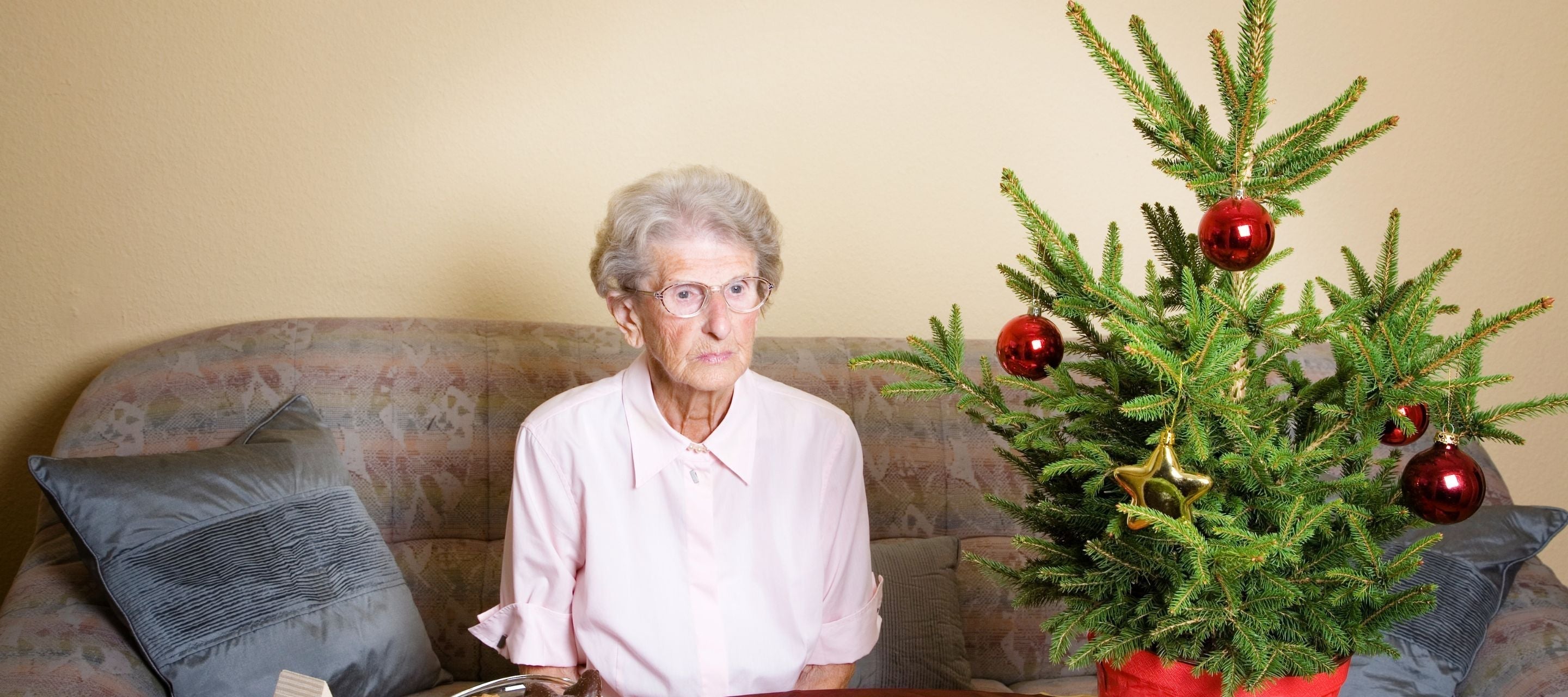 "An elderly woman sitting alone next to a small Christmas tree, highlighting the impact of loneliness and the importance of small gestures