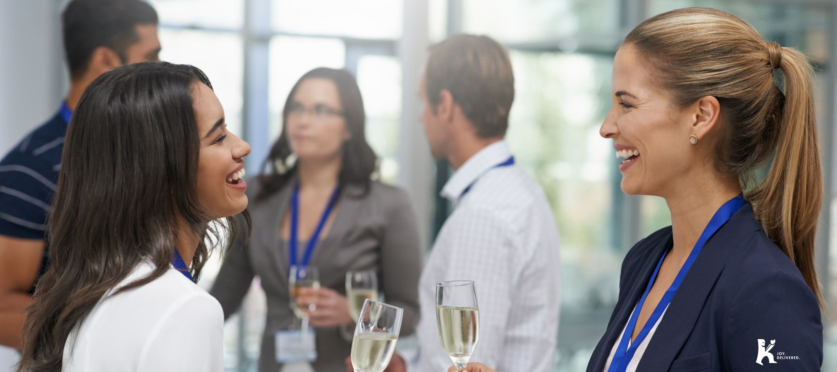 Professionals networking and laughing at a corporate event, holding glasses of sparkling wine, representing KULA’s corporate gifting options for clients, employees, and business partners.