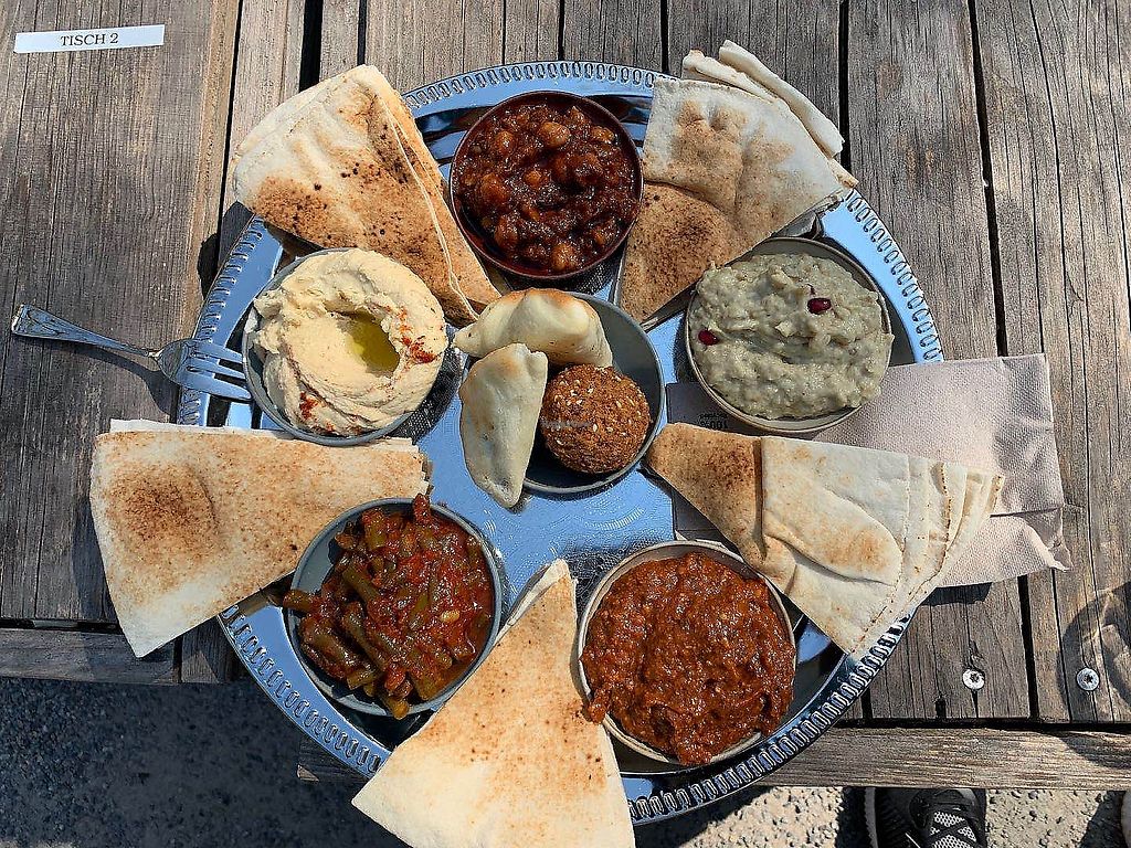 A delicious mezze platter from Kleine Freiheit café in Zürich, featuring hummus, baba ganoush, falafel, flatbread, and flavorful dips, served outdoors on a rustic wooden table. A perfect spot to enjoy fresh Mediterranean flavors.