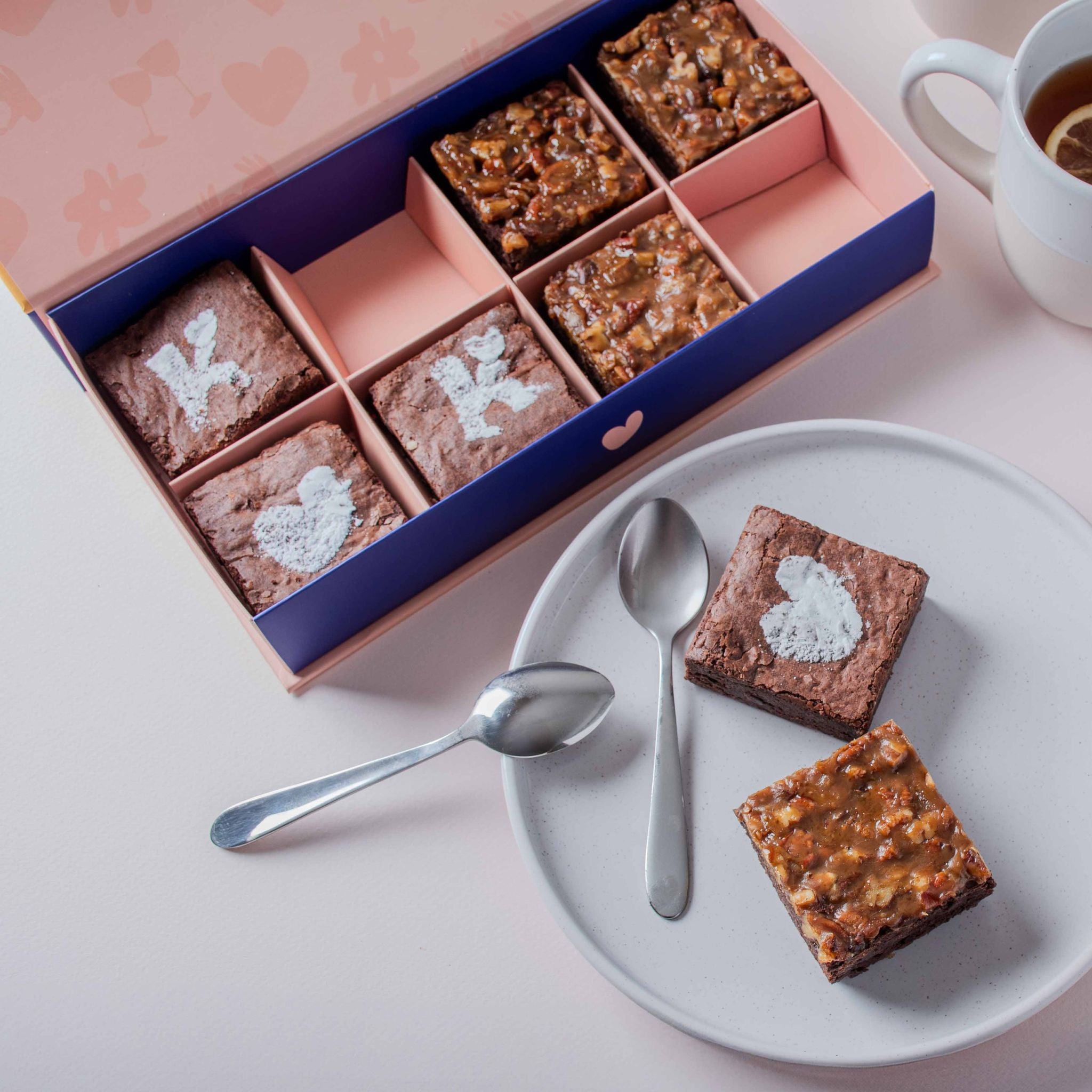 KULA Signature brownie gift box with a mix of classic chocolate and salted caramel brownies, featuring decorative powdered sugar designs, served with tea.