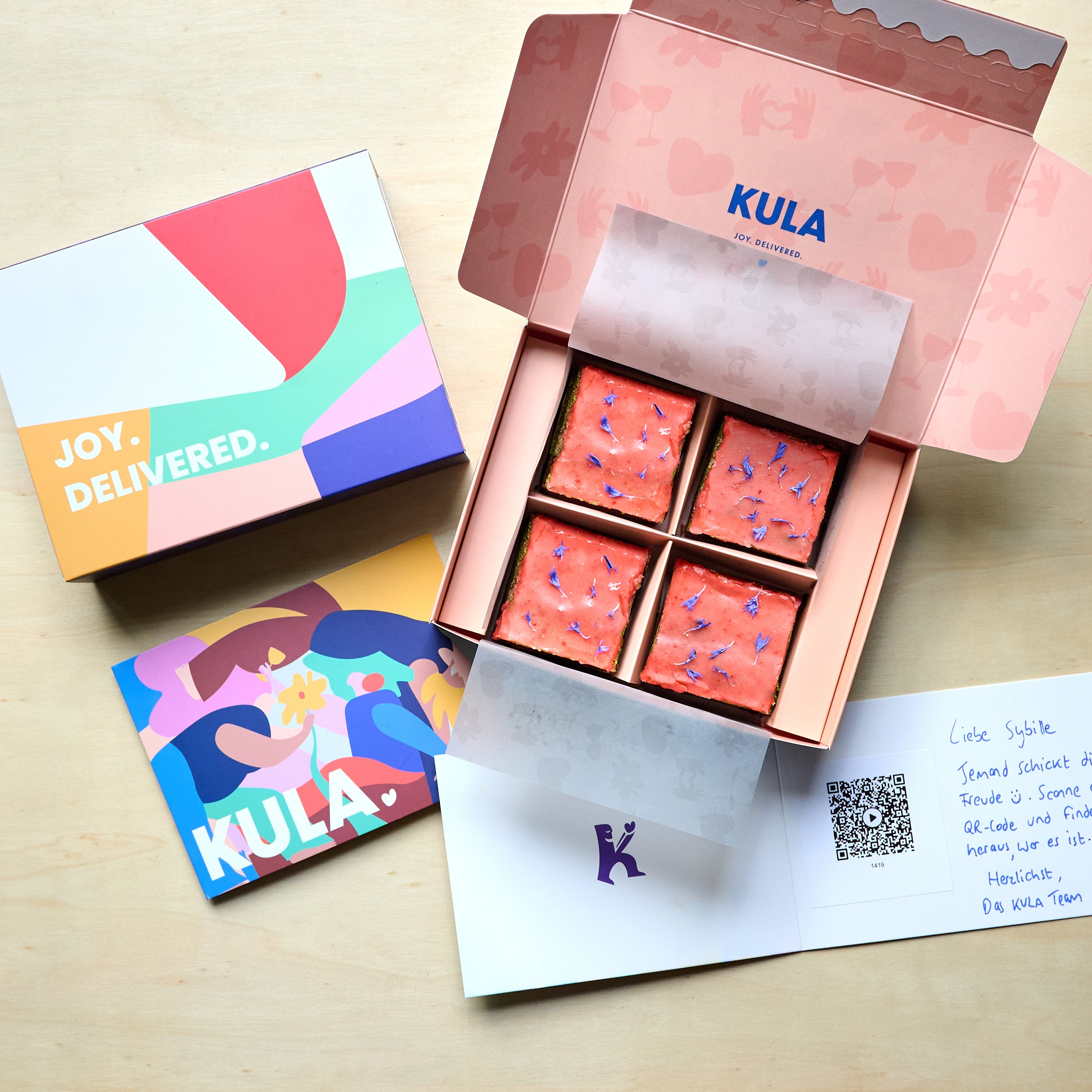 Open KULA gift box with 4 matcha-flavoured brownies topped with a strawberry glaze and a handwritten card.
