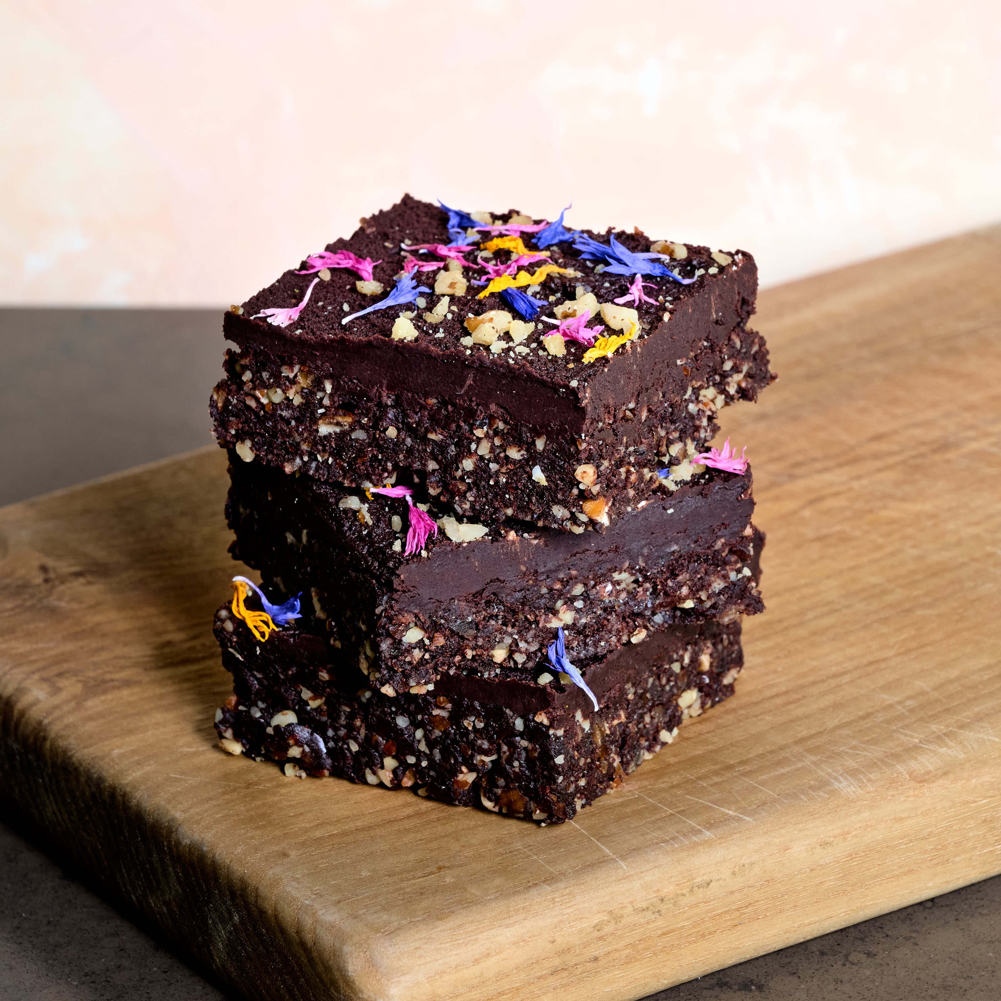 Stack of 3 KULA raw vegan brownies with a colorful edible flower and walnut pieces topping