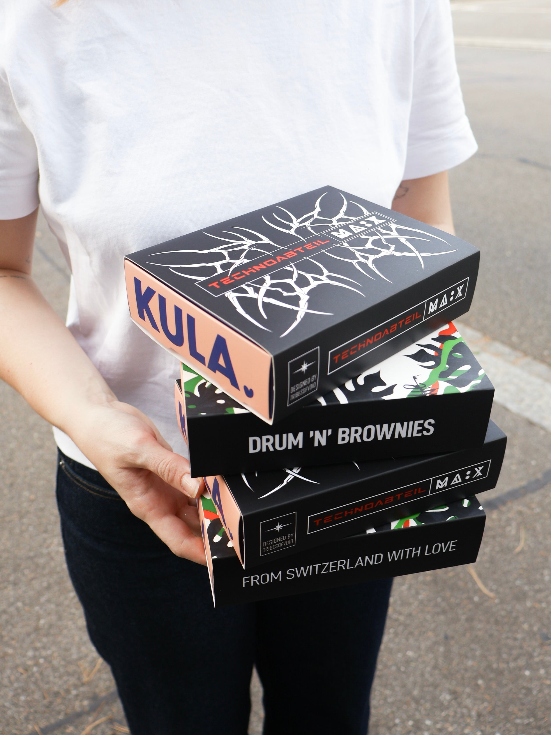 person holding four KULA boxes with different black sleeves for Technoabteil and MÄX